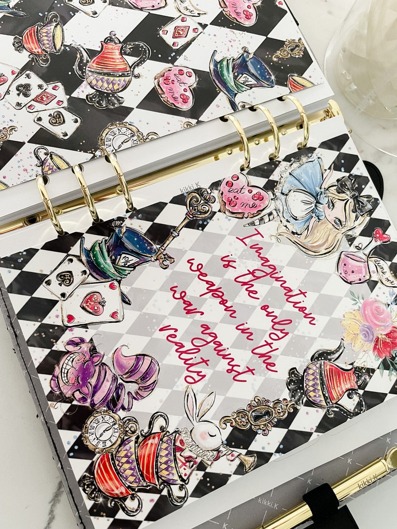 May include: A black and white checkered planner with a whimsical Alice in Wonderland theme. The planner features illustrations of Alice, the Mad Hatter, the Cheshire Cat, and other characters from the story. The text "Imagination is the only weapon in the war against reality" is printed on the cover.