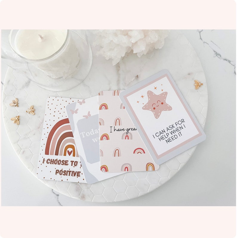 Puede incluir: Cinco tarjetas de afirmaci&oacute;n con mensajes positivos. Las tarjetas presentan un dise&ntilde;o de arco&iacute;ris con un coraz&oacute;n rosa y una estrella con una cara sonriente. El texto en las tarjetas dice: "Elijo ser positivo", "Hoy voy a", "Tengo genial", y "Puedo pedir ayuda cuando la necesito".