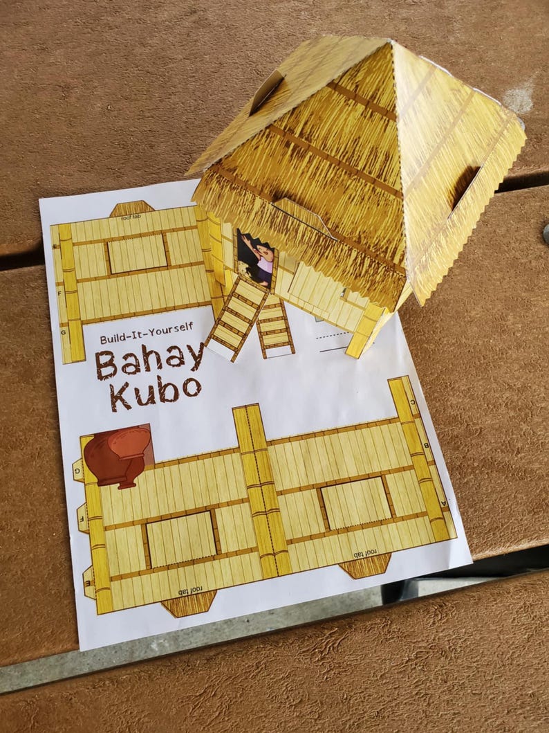 May include: A completed paper model of a Bahay Kubo, a traditional Filipino house, with a thatched roof and bamboo-style walls. The model is placed on top of the printed instructions. The text "Build-It-Yourself Bahay Kubo" is visible.