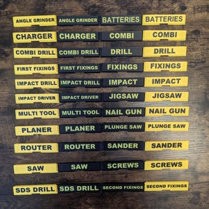 May include: A selection of black and yellow tool labels, each displaying a different tool name in a bold, sans-serif font. The labels include names such as "Angle Grinder", "Batteries", "Charger", and "Combi Drill".