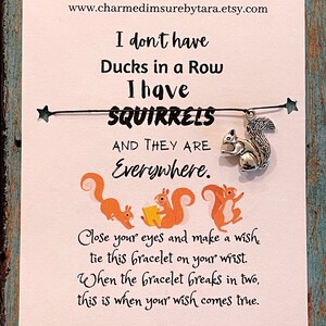 May include: A white card with a black string and a silver charm of a squirrel. The card has the text "I don't have Ducks in a Row I have SQUIRRELS AND THEY ARE Everywhere." and "Close your eyes and make a wish tie this bracelet on your wrist. When the bracelet breaks in two, this is when your wish comes true."