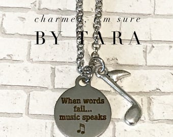 May include: Silver necklace with a charm that says "When words fail... music speaks" and a music note charm. The necklace is on a brick background.