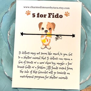 May include: A white card with a cartoon bulldog holding a yellow chew toy. The card says "5 for Fido" and "www.charmedimsurebytara.etsy.com". The text on the card reads: "5 dollars may not seem like much to you, but to a shelter animal that 5 dollars can mean a box of treats or a new chew toy, maybe a few tennis balls or a frisbee. All funds raised from the sale of this bracelet will go towards an enrichment program for shelter animals."