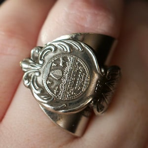 May include: A silver ring made from a repurposed spoon with an ornate design and a circular inscription. The inscription reads "Southwestern Bell Telephone Co."