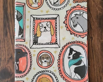 Può includere: Un tessuto beige con un motivo ripetuto di cani in cornici ovali. Le cornici sono contornate di nero e hanno un bordo rosa e turchese. I cani sono disegnati in stile cartone animato e indossano collari e bandane. Lo sfondo è beige chiaro con stelle dorate.