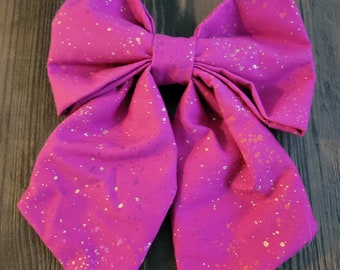 Peut inclure: Un grand nœud rose avec des accents de paillettes dorées. Le nœud est fait de tissu et a une forme pointue.