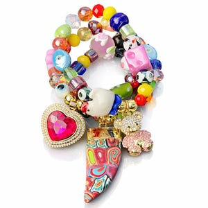 Puede incluir: Una colorida pulsera de cuentas con varios dijes. La pulsera presenta un dije en forma de corazón con una piedra preciosa rosa, un dije de oso de peluche y un colgante estampado. Las cuentas son de varios colores, incluyendo rojo, amarillo, azul y rosa.
