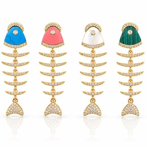 Puede incluir: Cuatro pendientes dorados con forma de espina de pescado, con cristales transparentes engastados a lo largo de la columna y la cola. Cada cabeza de pez tiene una piedra distinta: turquesa azul, rosa coral, nácar blanco y malaquita verde a rayas.