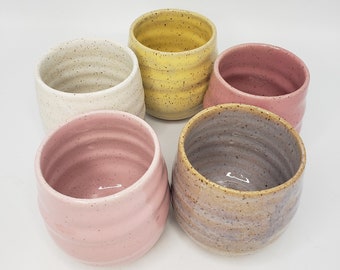 Può includere: Set di sei tazze in ceramica di vari colori, tra cui bianco, giallo, rosa e grigio. Ogni tazza ha una smaltatura macchiata e una forma arrotondata.