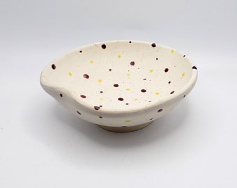 May include: A white ceramic bowl with a speckled design. The bowl has brown and yellow dots.