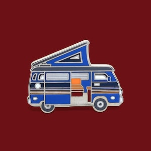 May include: Blue and white enamel pin of a vintage camper van with a pop-up top. The camper van has a striped design and orange accents.