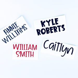 May include: Four white rectangular stickers with names printed in different colors and fonts. The names are Annie Williams, Kyle Roberts, William Smith, and Caitlyn. The text is in navy blue, red, and black.