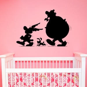 May include: Black silhouette wall decal of three cartoon characters, a large round character with a long nose, a smaller character with long ears, and a small dog-like character. The decal is on a pink wall above a white cot with a pink and white patterned bedding.