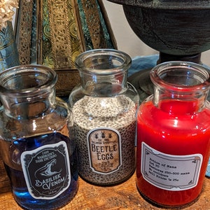 May include: Three glass bottles with labels and different colored liquids inside. The labels read "Basilisk Venom", "Beetle Eggs", and "Potion of Mana".
