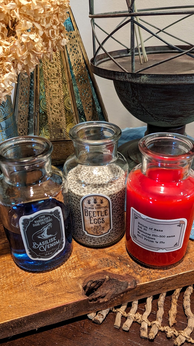 May include: Three glass bottles with labels and different colored liquids inside. The labels read "Basilisk Venom", "Beetle Eggs", and "Potion of Mana".