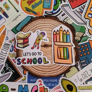May include: A collection of colorful school-themed stickers. The stickers feature images of pencils, books, and the text "Back to School" and "Let's Go to School". The stickers are arranged on a wooden slice.