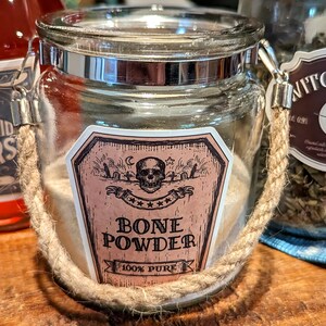 May include: A glass jar with a rope handle filled with a white powder. The jar has a label that says "Bone Powder 100% Pure" with a skull and crossbones graphic.