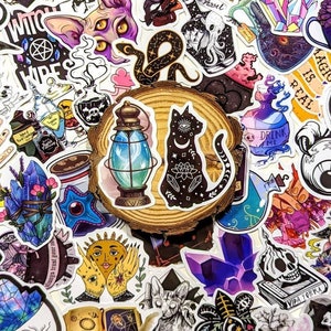 May include: A collection of colorful stickers featuring various witchy and mystical themes. The stickers include images of cats, snakes, skulls, crystals, potions, and other magical elements. The stickers are arranged on a wooden surface.