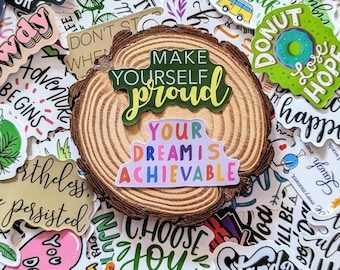 Può includere: Una collezione di adesivi colorati con messaggi motivazionali e ispiratori. Gli adesivi presentano frasi come "Renditi orgoglioso", "I tuoi sogni sono realizzabili", "Scegli la gioia" e "Stai con me".