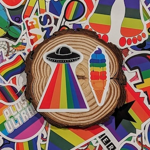 May include: A collection of rainbow-colored stickers featuring various designs, including a UFO, an ice cream cone, a crown, and footprints. The stickers are arranged on a wooden surface.