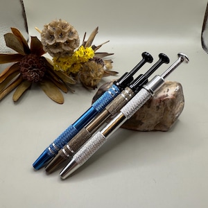 May include: Three metal tools with textured handles and black tips. The tools are arranged on a rock with a light brown and grey colour.
