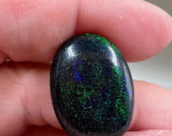 May include: A black oval opal gemstone with green and blue iridescent flashes.