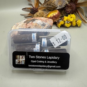 May include: A clear plastic case containing several lapidary tools. The tools are cylindrical with a dark grey abrasive surface and metal shafts. A label on the case reads "Two Stones Lapidary" and "Opal Cutting & Jewellery". The price tag shows £12.00.
