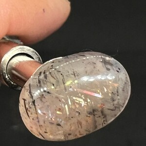 May include: A clear, oval-shaped gemstone with black inclusions. The gemstone is set in a silver setting and is mounted on a silver post.