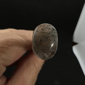 May include: A clear oval-shaped gemstone with black and brown inclusions. The gemstone is translucent and has a smooth, polished surface.