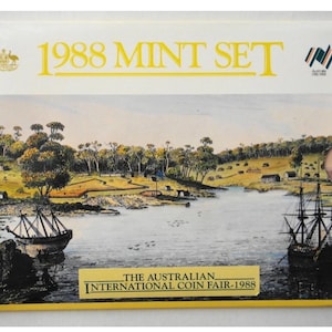 May include: A rectangular 1988 Mint Set coin collection folder featuring a landscape illustration of a harbour with sailing ships, trees, and buildings. The text reads 1988 MINT SET and THE AUSTRALIAN INTERNATIONAL COIN FAIR-1988 with the Australian coat of arms.