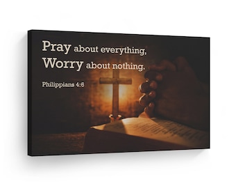 May include: A canvas print with a dark background featuring a pair of hands clasped in prayer over an open book and a glowing cross. The text "Pray about everything, Worry about nothing. Philippians 4:6" is displayed in a light beige font.