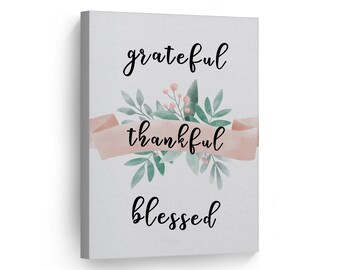 May include: A watercolor painting with a pink ribbon and green leaves. The ribbon has the words "thankful" written on it. The words "grateful" and "blessed" are written above and below the ribbon.