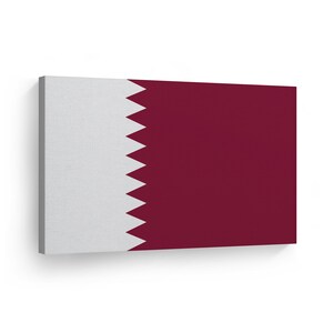 May include: A canvas print of the flag of Qatar. The flag is white with a maroon rectangle on the right side and a jagged maroon triangle on the left side.