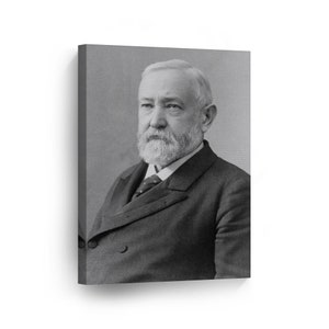 May include: A black and white portrait of a man with a thick white beard and mustache. He is wearing a dark suit with a white shirt and a patterned tie. The man is looking directly at the camera.