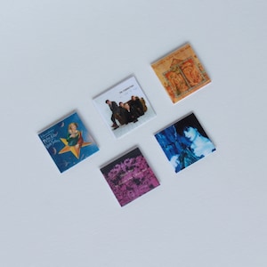 May include: Five different album covers, each with a unique design. The covers are all square and have a white background. The album covers are arranged in a grid pattern. The album covers feature a variety of images, including a group of people, a woman in a blue dress, a woman in a yellow dress, and a floral design.