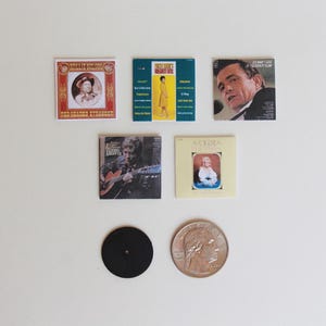 May include: A collection of five vintage vinyl record covers featuring various artists and album titles. The covers are in various colors and feature images of musicians and album titles. There is also a black vinyl record and a silver US quarter.