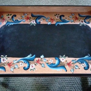 Puede incluir: Una bandeja de servir de madera con un centro pintado de negro y un borde floral decorativo pintado en azul, rojo y blanco.