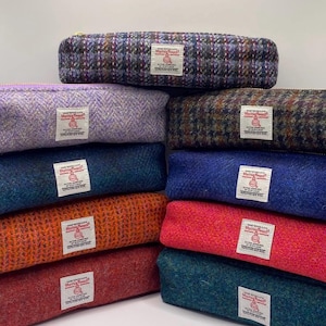 May include: A collection of colourful pencil cases made from textured fabric. The cases are in shades of purple, blue, orange, and red. Each case features a zip closure and a small label.
