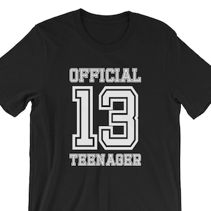 May include: Black t-shirt with white text that reads "OFFICIAL 13 TEENAGER" in a varsity style font.