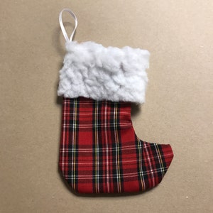 May include: A small red and black plaid Christmas stocking with a white faux fur cuff and a white loop for hanging.