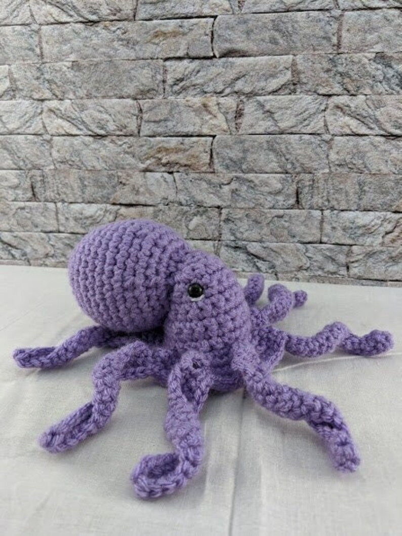 May include: A crocheted purple octopus plush toy with eight tentacles. The octopus has a single black eye.