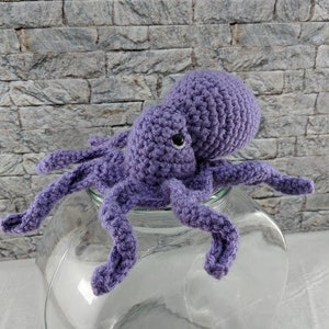 May include: A crocheted purple octopus with eight tentacles, sitting on a clear glass jar.
