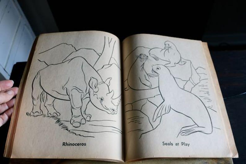 May include: Open book with black and white illustrations of animals. One page shows a rhinoceros with the word "Rhinoceros" below. The other page depicts seals with the text "Seals at Play".