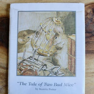 May include: A book cover featuring an illustration from "The Tale of Two Bad Mice" by Beatrix Potter. The image depicts two mice near a tipped-over birdcage and overturned furniture. The book cover is white with a light blue border.