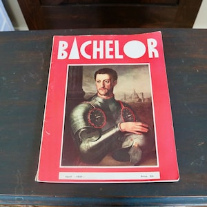 May include: Vintage "Bachelor" magazine from April 1937, featuring a portrait of a man in armor on the cover. The magazine has a red border with the title in white letters. The magazine is resting on a dark wooden surface.