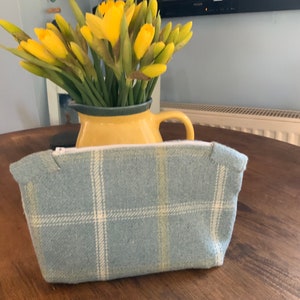 May include: A blue and white plaid zippered pouch with a white zipper pull. The pouch is sitting on a wooden table.