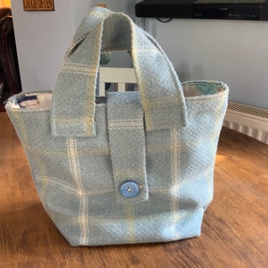 May include: A light blue tote bag with a white and yellow plaid pattern. The bag has a single button closure and two fabric handles.