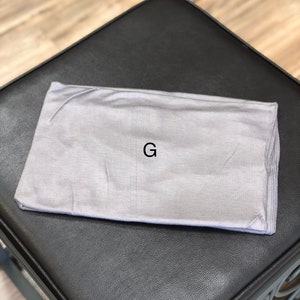 Puede incluir: Una diadema gris con la letra "G" impresa en ella.