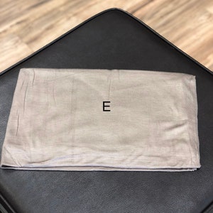 Puede incluir: Una bolsa de tela gris claro con la letra "E" impresa en negro en la parte delantera.