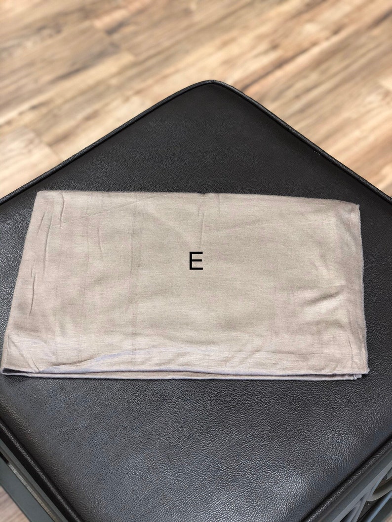 Puede incluir: Una bolsa de tela gris claro con la letra "E" impresa en negro en la parte delantera.